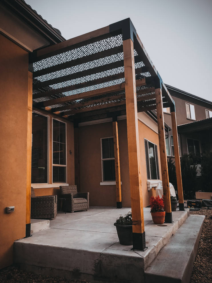 This is an example of a large modern back patio in Denver with stamped concrete and a pergola.