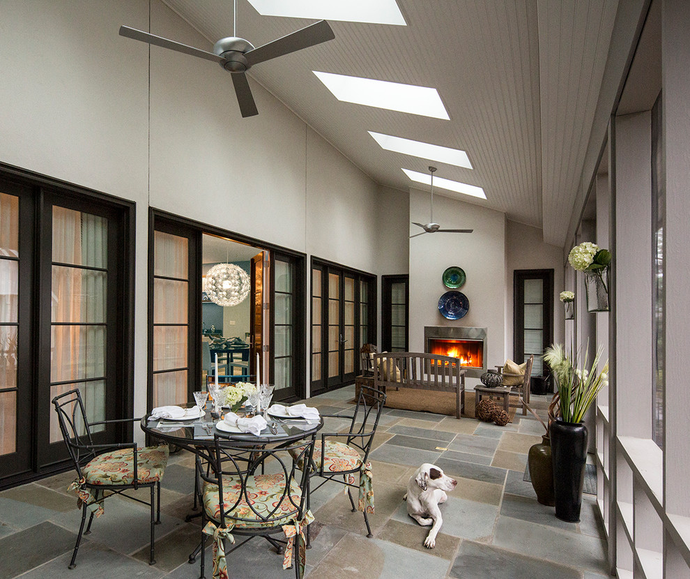 Réalisation d'une grande terrasse arrière design avec un foyer extérieur, des pavés en pierre naturelle et une extension de toiture.