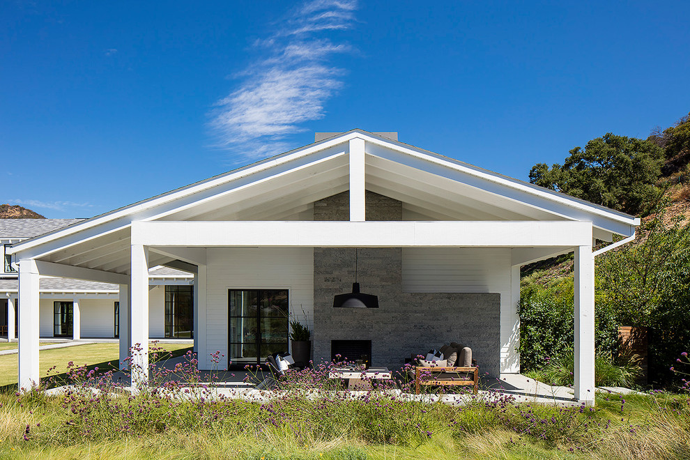 This is an example of a farmhouse back patio in Los Angeles with concrete slabs, a roof extension and a fireplace.