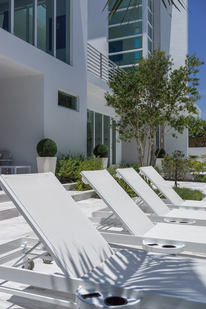 Design ideas for an expansive contemporary front patio in Miami with natural stone paving and no cover.