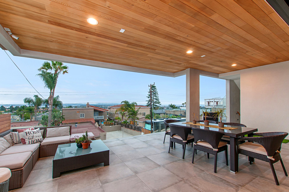 Cette image montre une grande terrasse arrière minimaliste avec des pavés en béton et une extension de toiture.