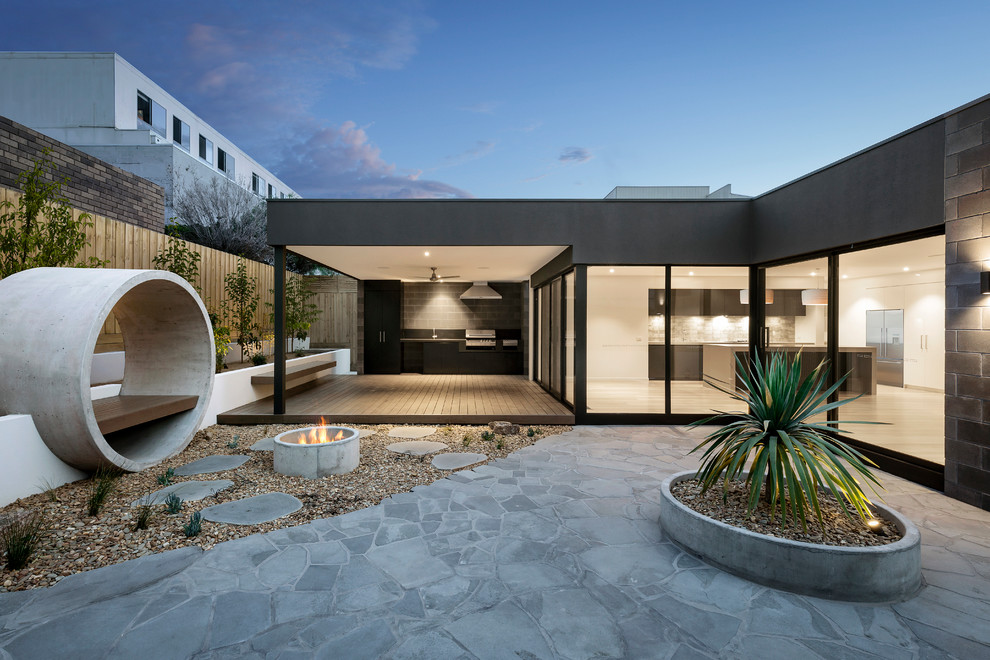 Cette image montre une terrasse design avec un foyer extérieur, des pavés en pierre naturelle et une extension de toiture.