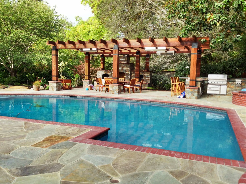 Cette photo montre une grande terrasse arrière méditerranéenne avec une cuisine d'été, des pavés en pierre naturelle et une pergola.