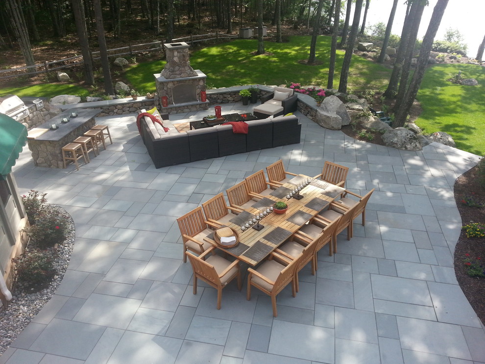 Réalisation d'une grande terrasse arrière tradition avec un foyer extérieur, des pavés en pierre naturelle et aucune couverture.