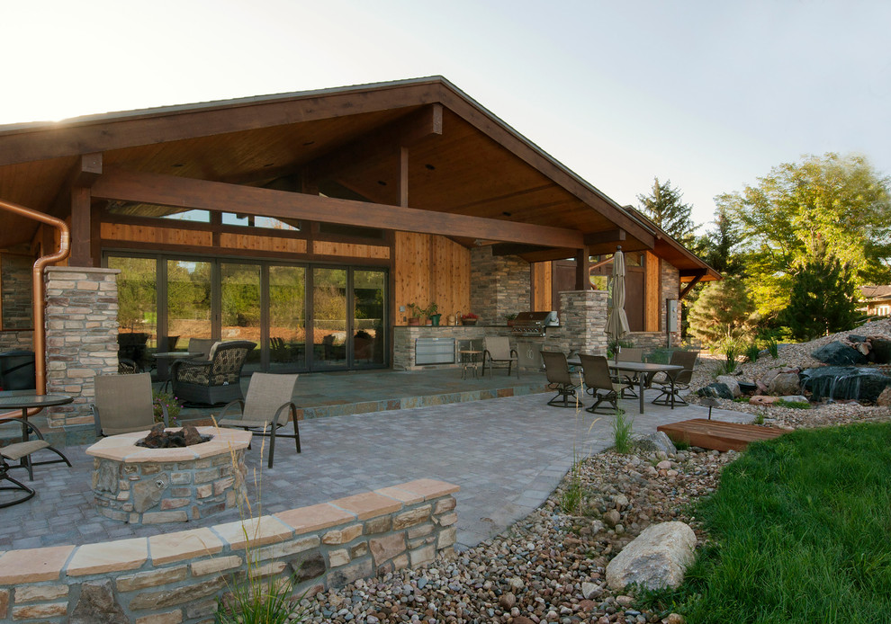 Cette image montre une terrasse arrière craftsman avec une cuisine d'été, des pavés en pierre naturelle et une extension de toiture.
