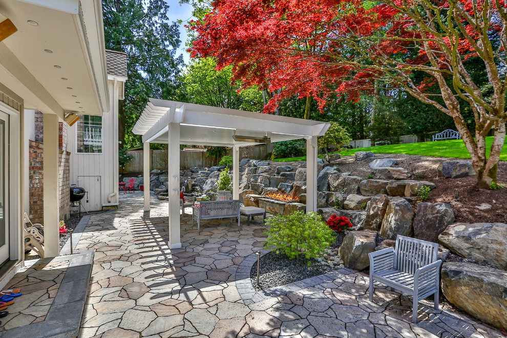 Diseño de patio clásico renovado de tamaño medio en patio trasero con brasero, adoquines de piedra natural y pérgola
