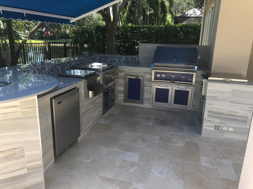 Photo of a world-inspired back patio in Miami with an outdoor kitchen, natural stone paving and an awning.