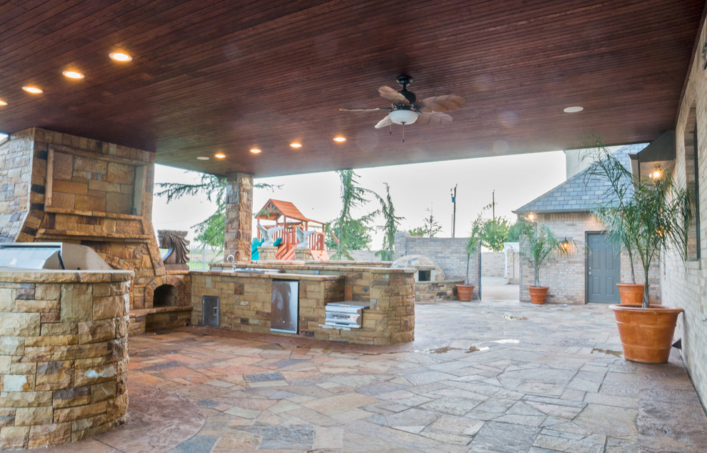 Expansive classic back patio in Oklahoma City with an outdoor kitchen, natural stone paving and a roof extension.