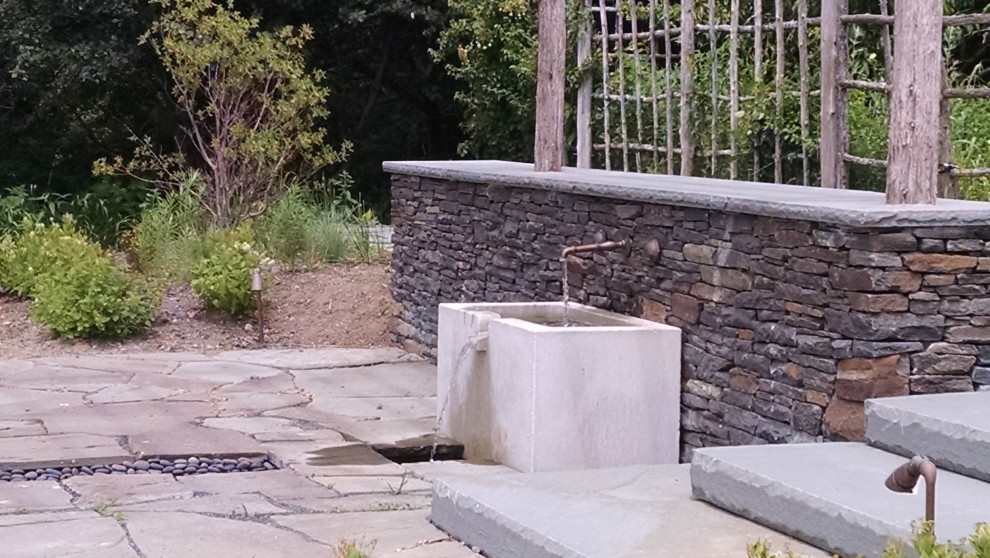 Réalisation d'une terrasse arrière tradition avec un point d'eau, des pavés en pierre naturelle et une pergola.
