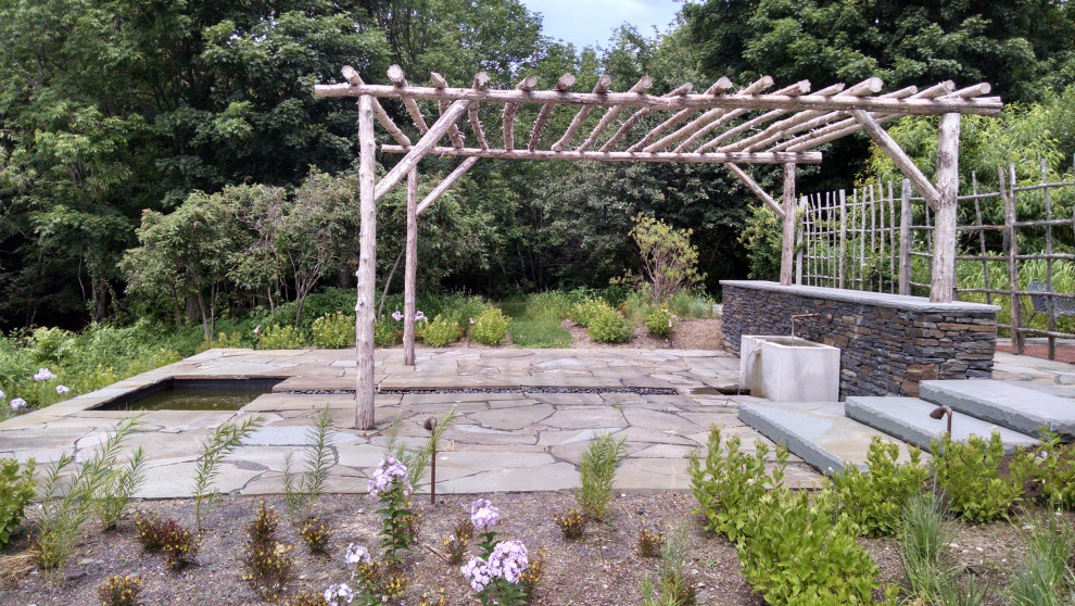Inspiration for a traditional back patio in New York with natural stone paving, a water feature and a pergola.