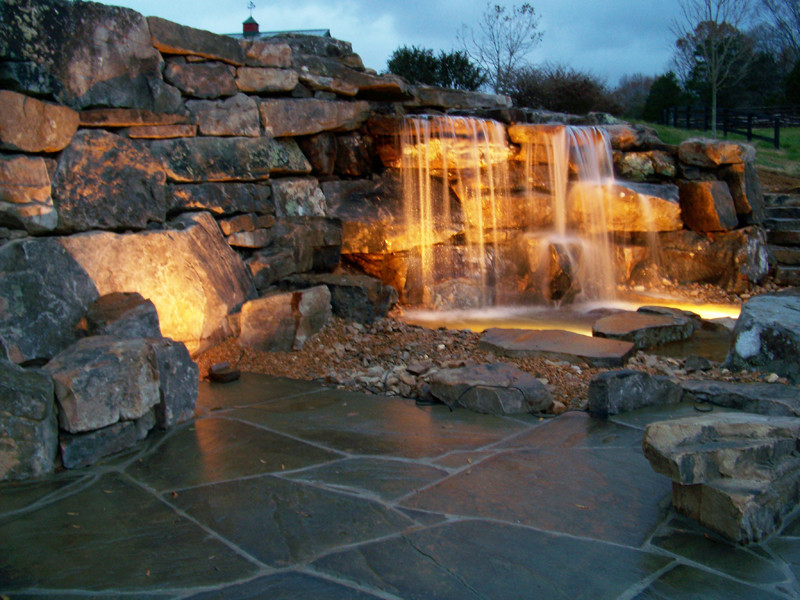 Example of a mountain style side yard stone patio fountain design in Other