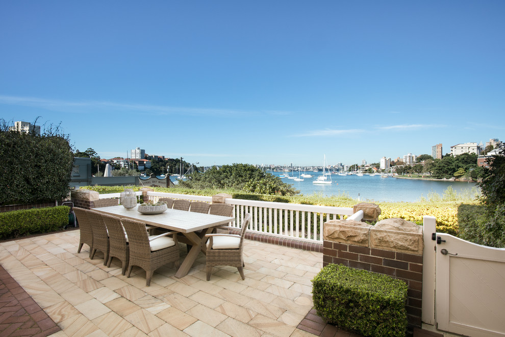 This is an example of a large coastal back patio in Sydney with natural stone paving and no cover.