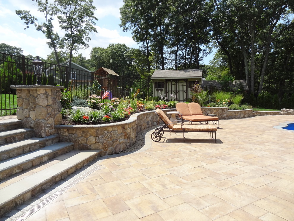 Design ideas for a large traditional back patio in New York with a potted garden, natural stone paving and no cover.