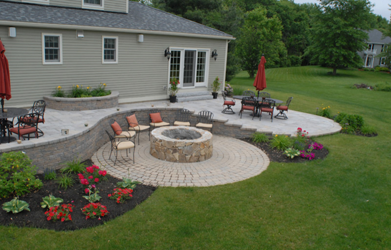 This is an example of a large traditional back patio in Boston with a fire feature, natural stone paving and no cover.