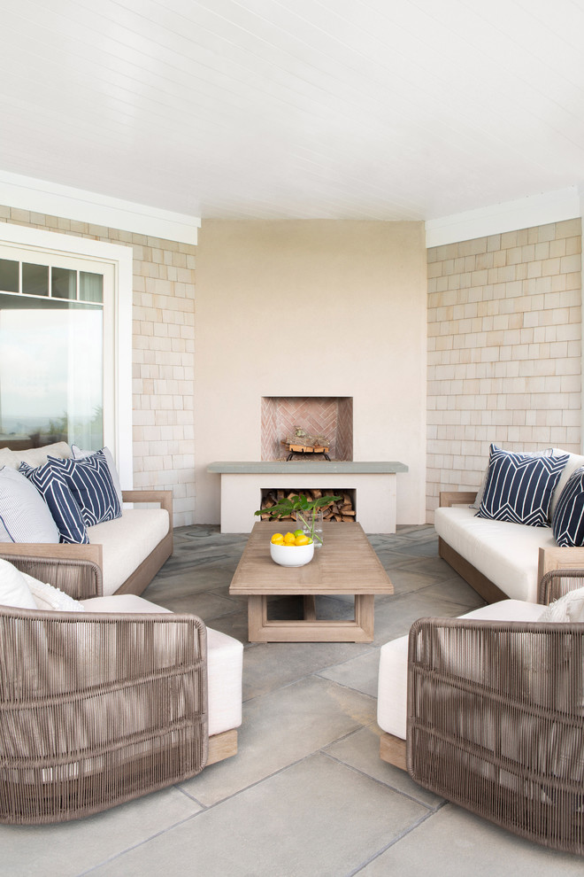 Example of a large beach style backyard concrete paver patio design in New York with a fireplace and a roof extension