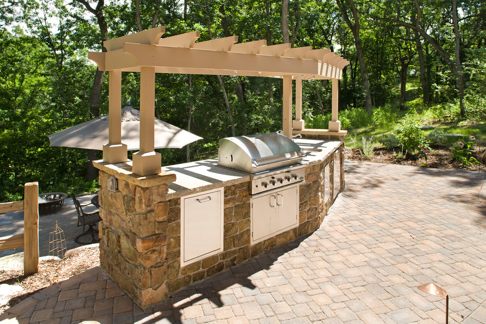 Photo of a large classic back patio in Minneapolis with an outdoor kitchen, brick paving and a pergola.