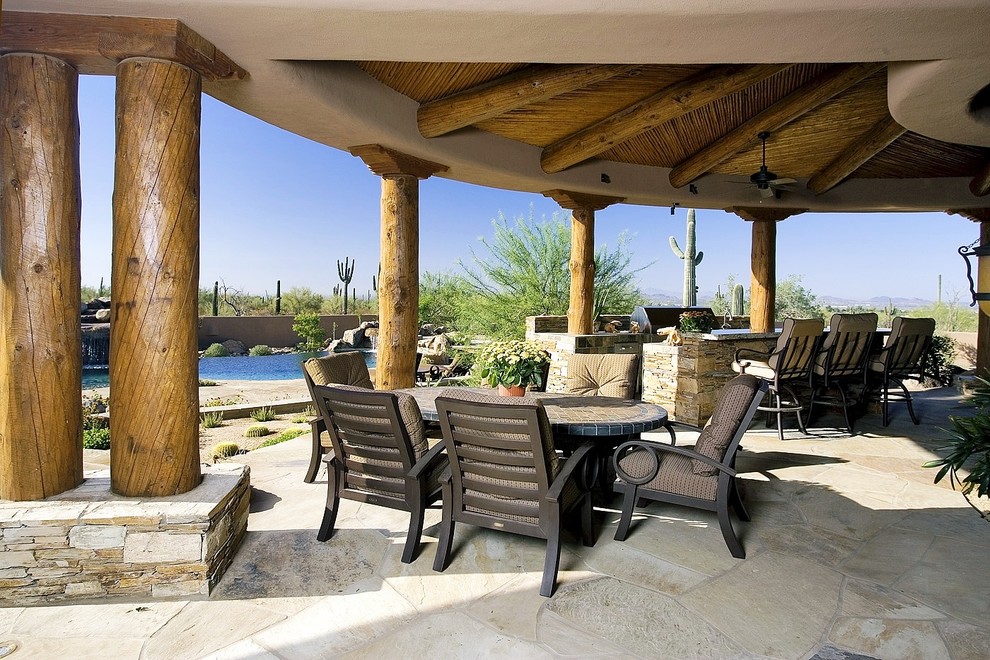 Cette image montre une très grande terrasse arrière sud-ouest américain avec une cuisine d'été, des pavés en pierre naturelle et une extension de toiture.