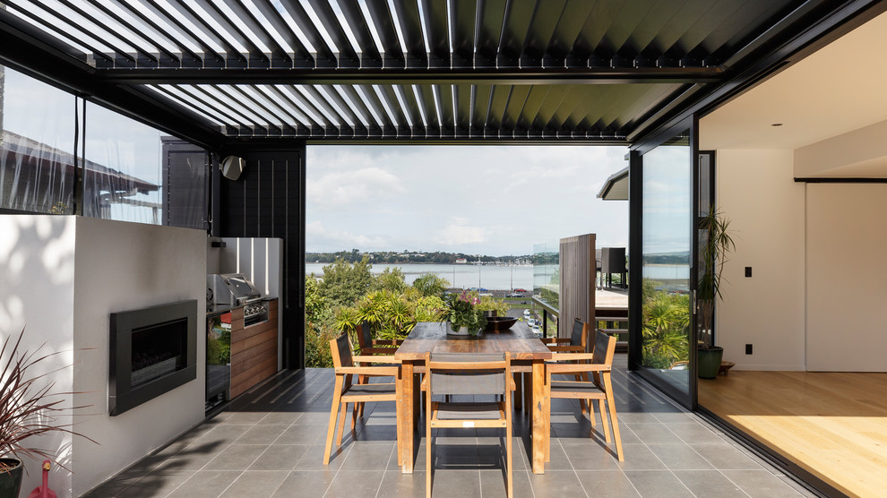 Patio - contemporary side yard tile patio idea in Auckland with a pergola and a fireplace