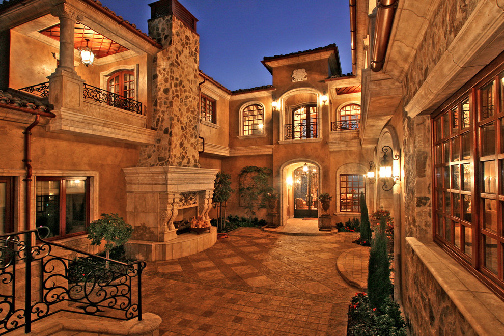 Пример оригинального дизайна: большой двор на внутреннем дворе в средиземноморском стиле с уличным камином и покрытием из каменной брусчатки без защиты от солнца