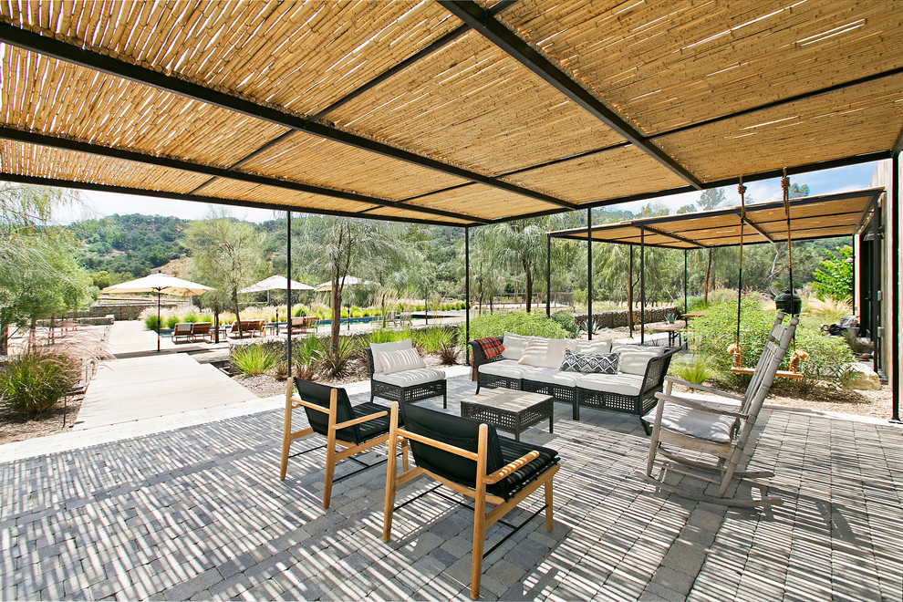 Diseño de patio de estilo de casa de campo en patio trasero con adoquines de hormigón y pérgola