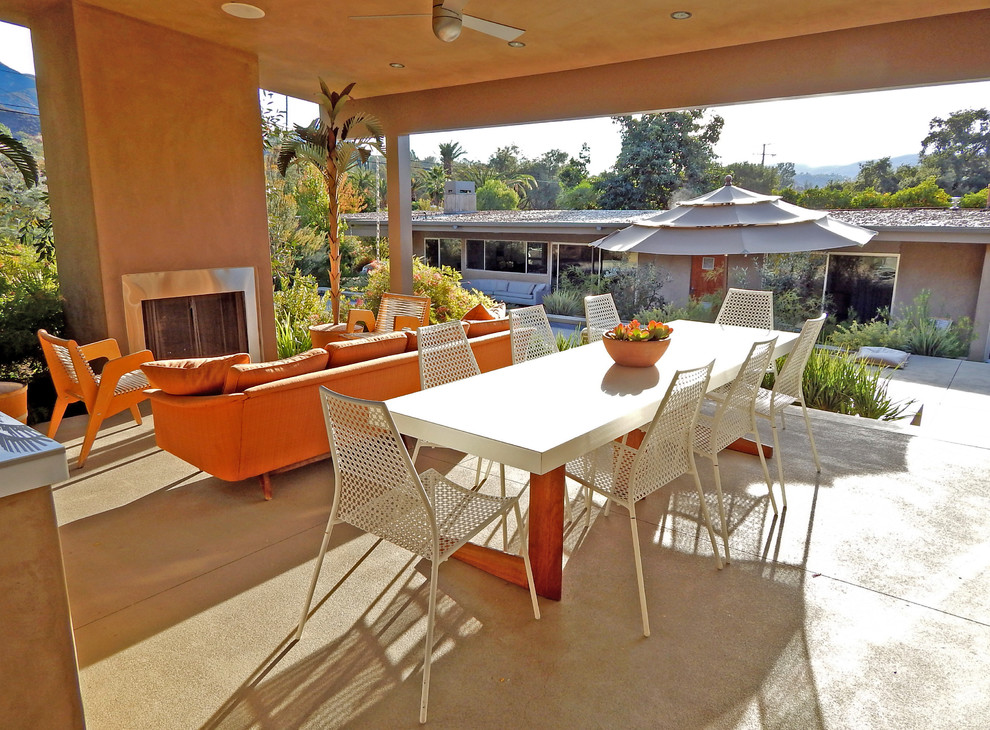Inspiration for a large midcentury back patio in Los Angeles with a fire feature, concrete slabs and a roof extension.