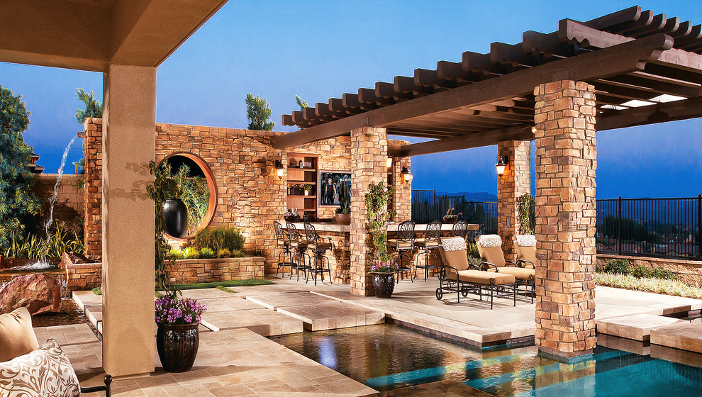 This is an example of a large mediterranean back patio in Los Angeles with an outdoor kitchen, concrete slabs and a pergola.