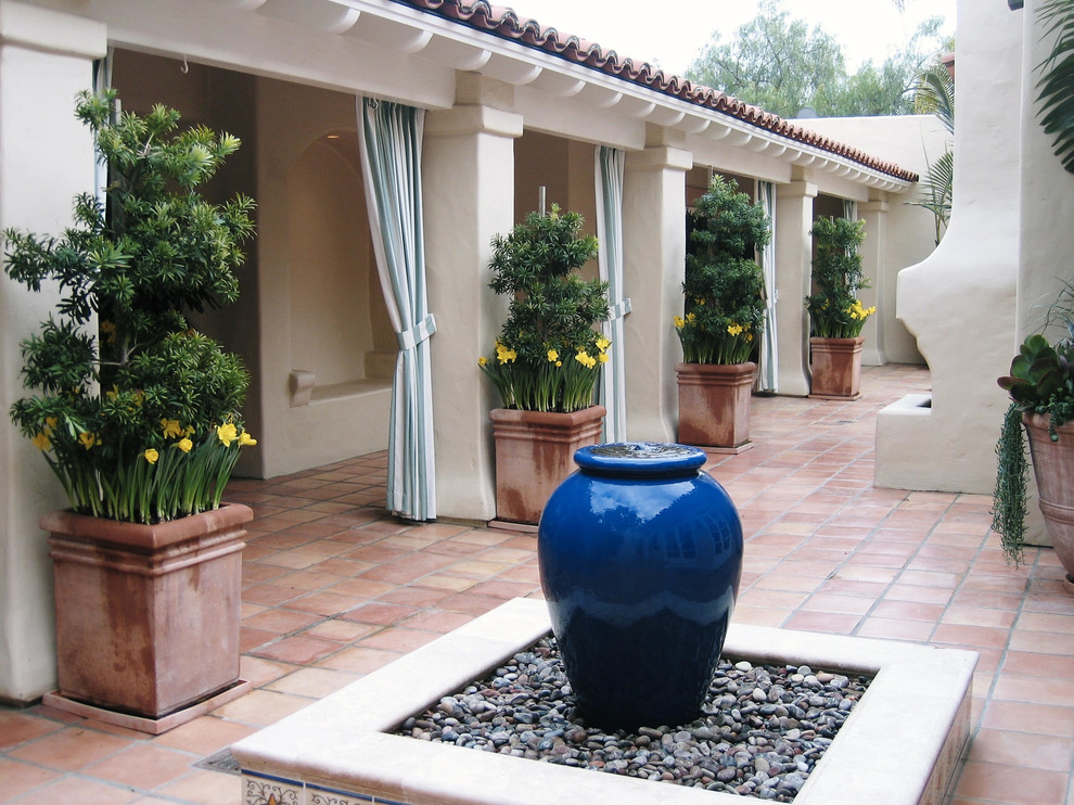 Foto di un grande patio o portico mediterraneo dietro casa con fontane, piastrelle e un tetto a sbalzo
