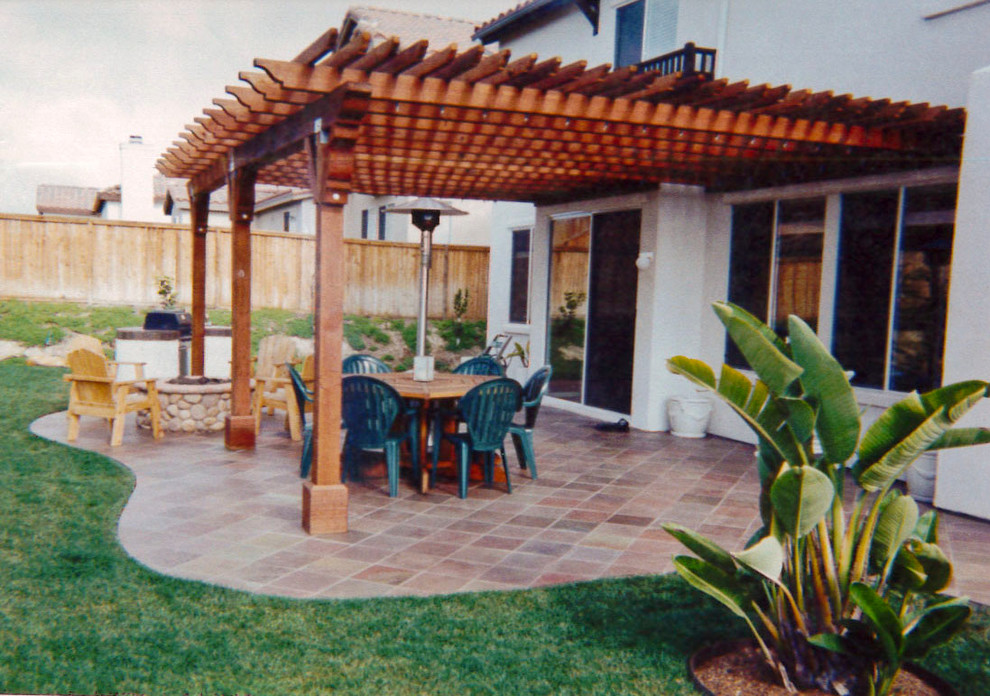 Cette photo montre une grande terrasse arrière exotique avec une cuisine d'été, des pavés en pierre naturelle et une pergola.