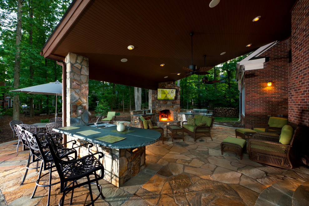 This is an example of a large rustic back patio in Charlotte with natural stone paving, a gazebo and an outdoor kitchen.