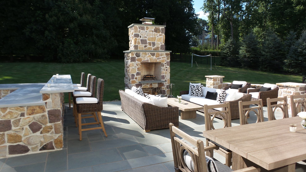 This is an example of a large modern back patio in Philadelphia with an outdoor kitchen and natural stone paving.