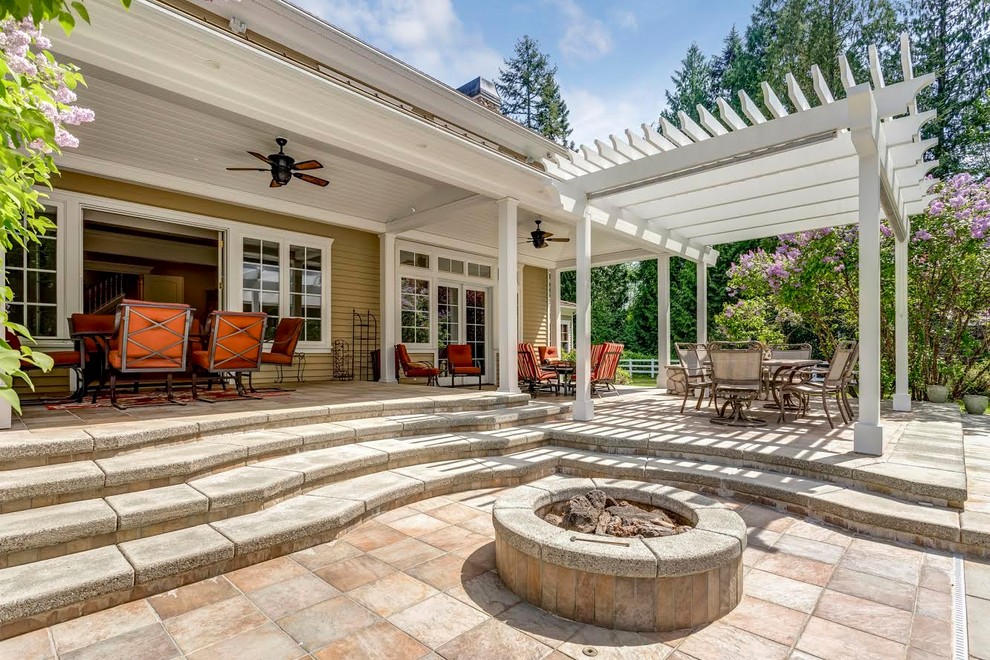 Immagine di un grande patio o portico classico dietro casa con un focolare, pavimentazioni in pietra naturale e un tetto a sbalzo