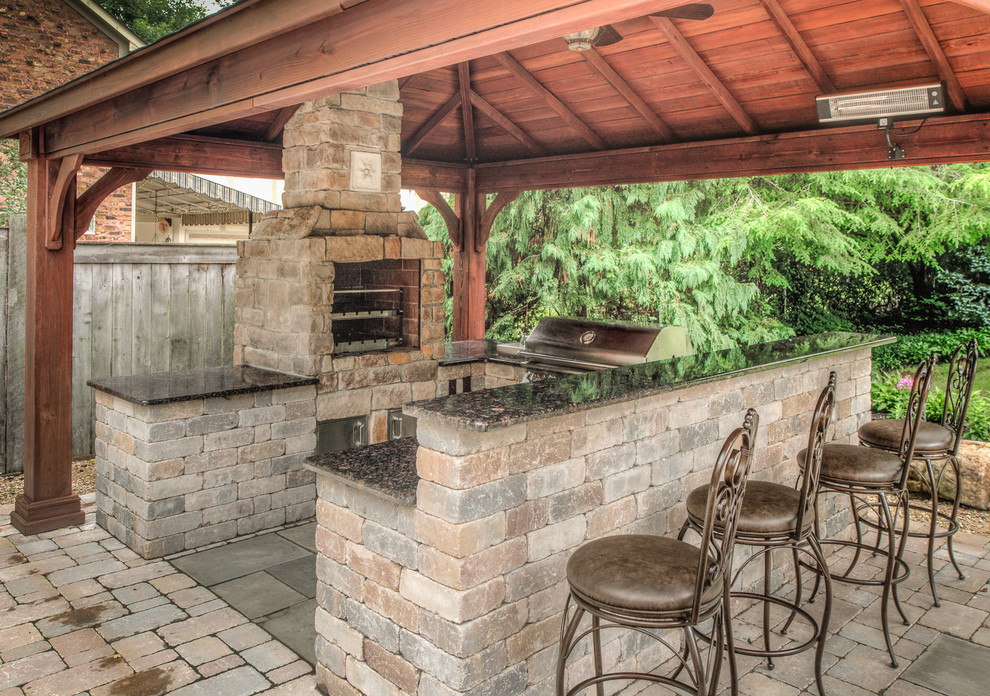 Cette photo montre une terrasse arrière chic de taille moyenne avec une cuisine d'été, des pavés en brique et une pergola.