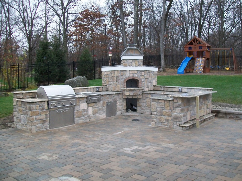 This is an example of a large traditional back patio in New York with an outdoor kitchen, concrete paving and no cover.