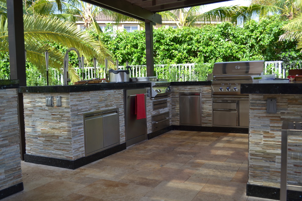 This is an example of an expansive mediterranean back patio in Miami with an outdoor kitchen, natural stone paving and a pergola.