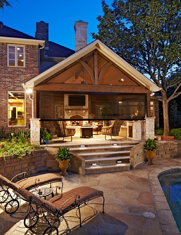 Réalisation d'une grande terrasse arrière tradition avec une cuisine d'été, une extension de toiture et des pavés en pierre naturelle.