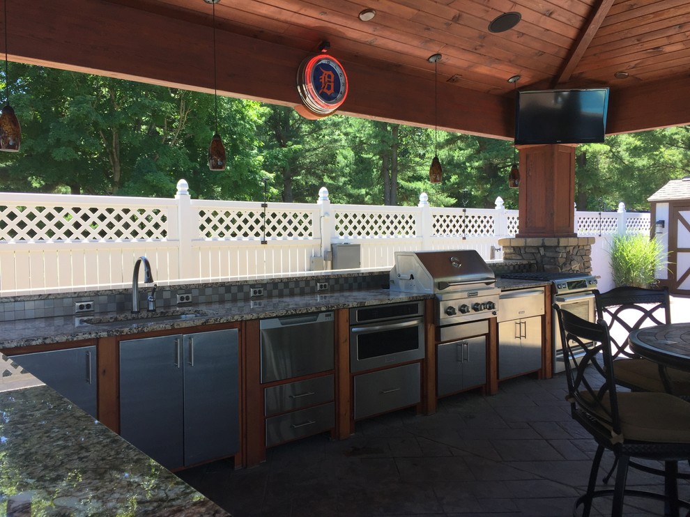 This is an example of a large classic back patio in Grand Rapids with an outdoor kitchen, stamped concrete and a pergola.