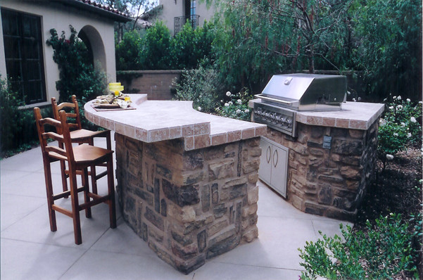 This is an example of a large classic back patio in Orange County with an outdoor kitchen, concrete slabs and no cover.