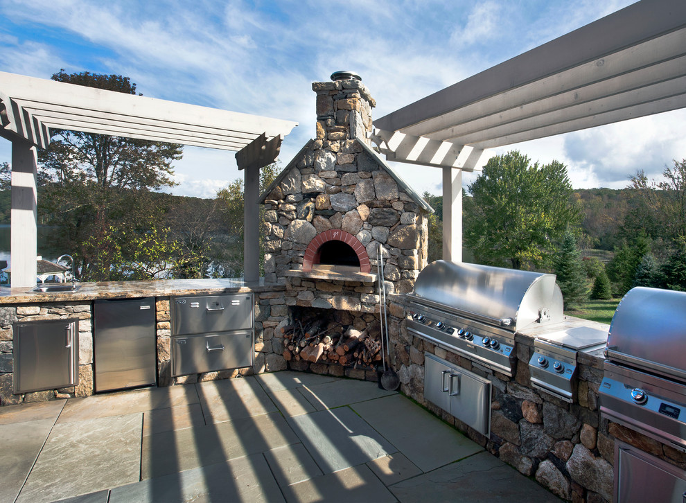 Huge farmhouse backyard stone patio kitchen photo in New York with a pergola