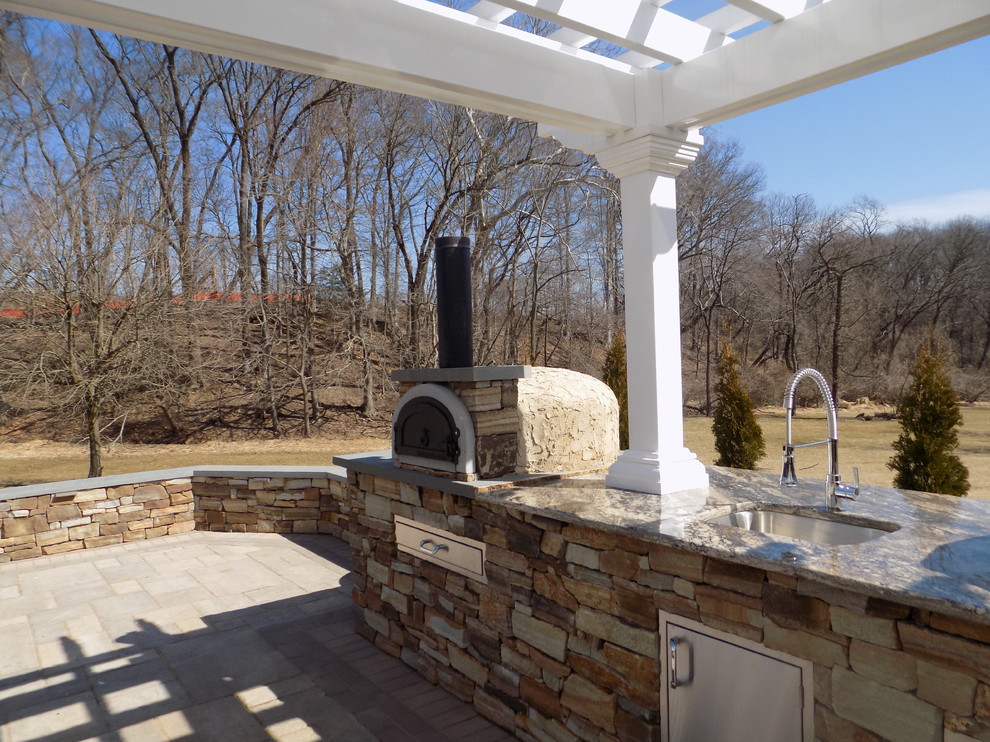 Aménagement d'une grande terrasse arrière moderne avec une cuisine d'été, des pavés en pierre naturelle et un auvent.