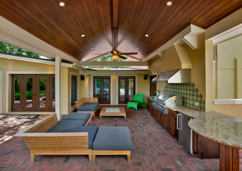 Cette image montre une grande terrasse arrière traditionnelle avec une cuisine d'été, des pavés en brique et une extension de toiture.