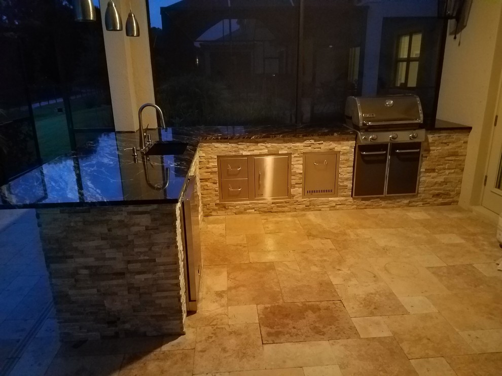 This is an example of a medium sized rustic back patio in Tampa with an outdoor kitchen, natural stone paving and a roof extension.