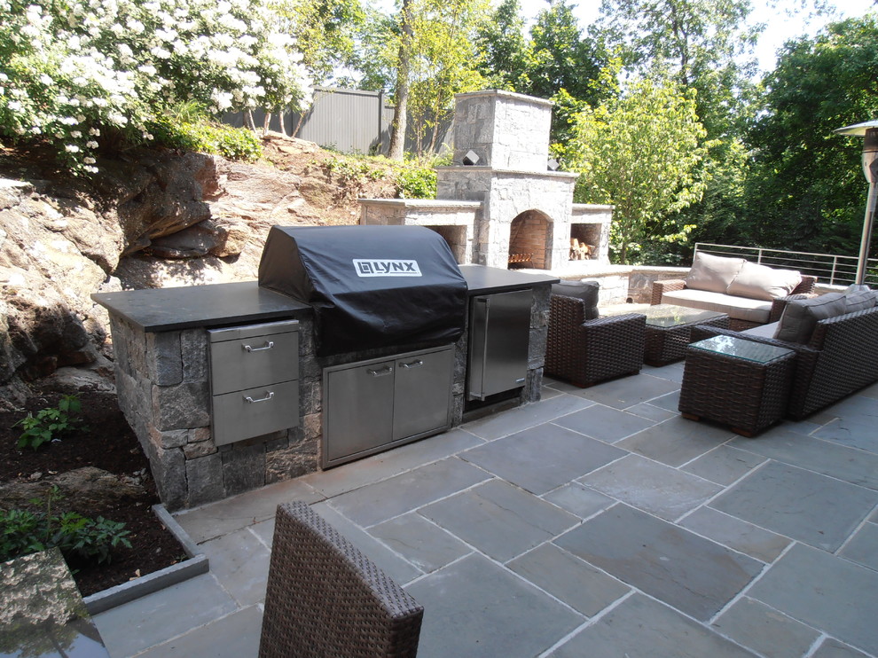 This is an example of a large modern back patio in New York with a fire feature, natural stone paving and no cover.