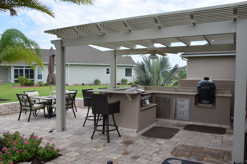 Cette photo montre une grande terrasse arrière chic avec une cuisine d'été, des pavés en béton et une pergola.