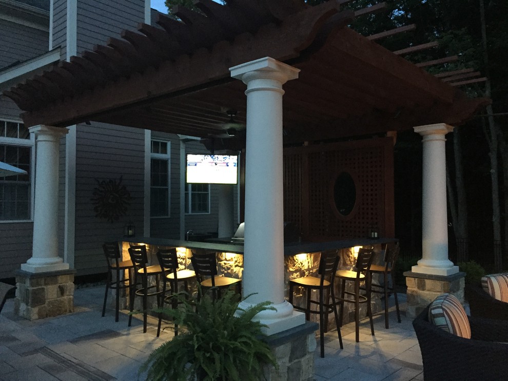 Idée de décoration pour une très grande terrasse arrière tradition avec une cuisine d'été, une pergola et des pavés en pierre naturelle.