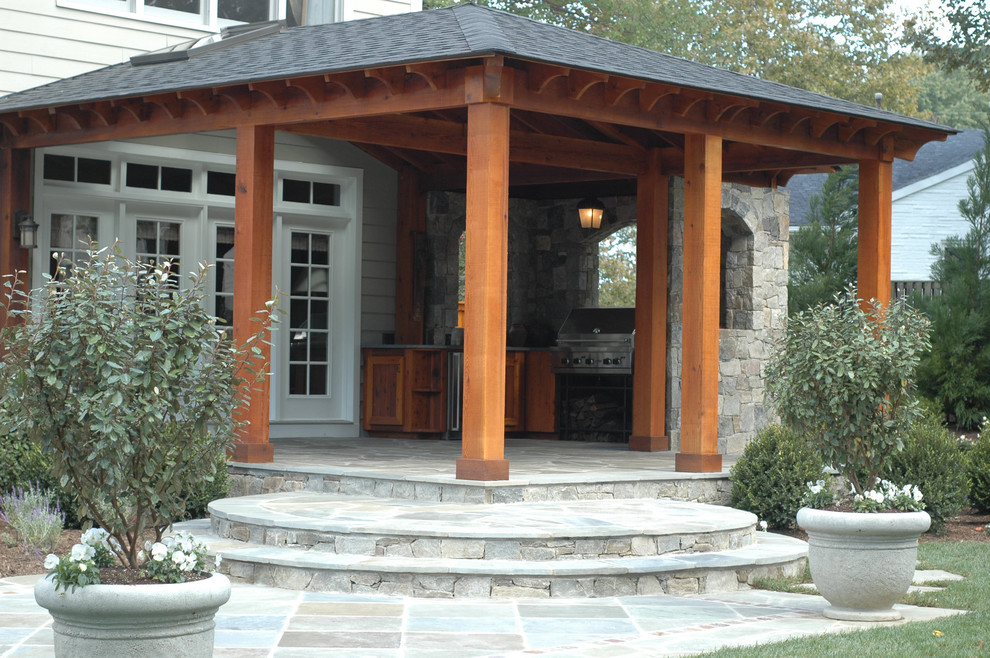 Cette image montre une grande terrasse arrière minimaliste avec une cuisine d'été, des pavés en pierre naturelle et une pergola.