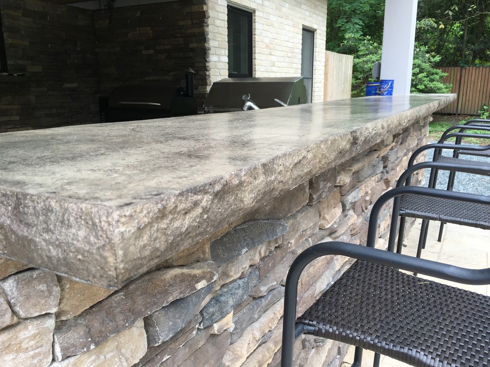 This is an example of a classic back patio in Houston with an outdoor kitchen, stamped concrete and a roof extension.