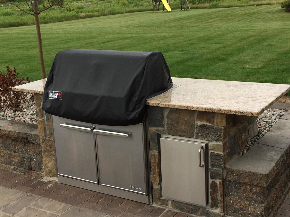This is an example of a traditional back patio in Grand Rapids with an outdoor kitchen, brick paving and no cover.