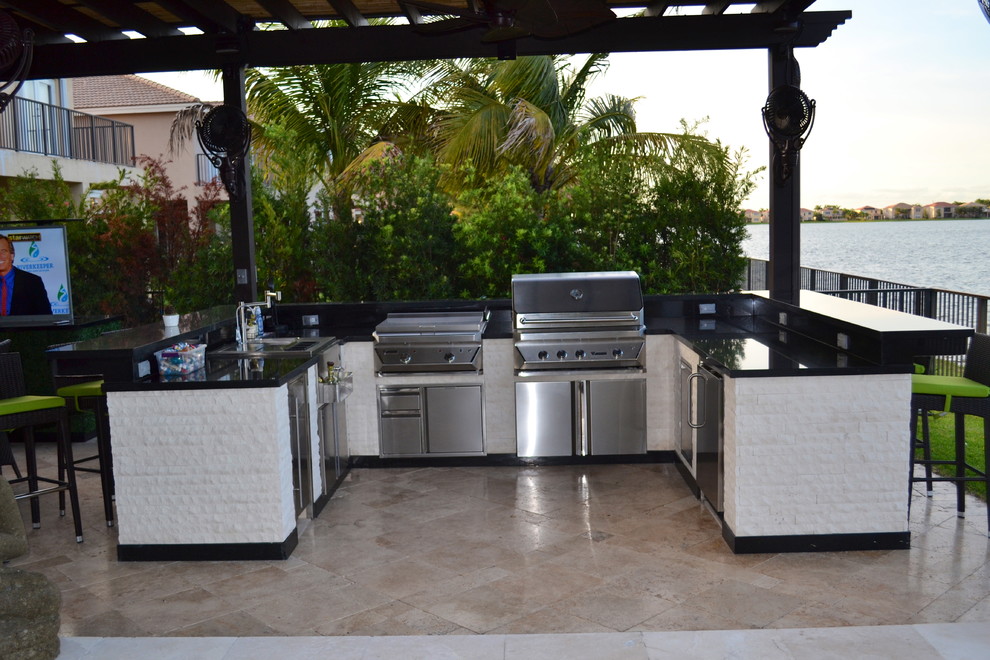 Patio kitchen - huge modern backyard stone patio kitchen idea in Miami with a pergola