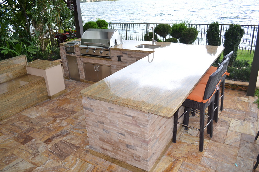 Huge elegant backyard stone patio kitchen photo in Miami with a pergola