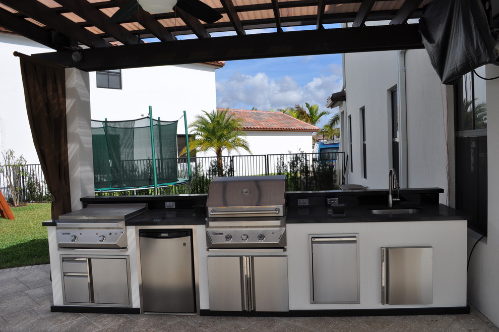 Example of a huge minimalist backyard stone patio kitchen design in Miami with a pergola